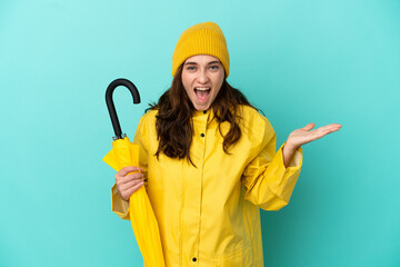 Young caucasian man holding an umbrella isolated on blue background with shocked facial expression