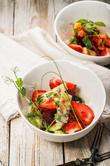 Vertical shot delicious summer salad. Salad with fresh strawberries, baked beets, yellow tomatoes, dor blue cheese and herbs in a white bowl on a light rustic background. Summerfood. Close-up