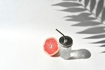 Fototapeta na wymiar Mock up summer still life vacation scene. Cocktail glass and cut grapefruit on white background in sunlight. Trendy minimalist concept. Palm leaves harsh shadows. High angle, copy space.