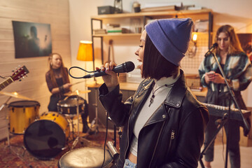 Fototapeta na wymiar Stylish female singing in microphone while ecording song in studio