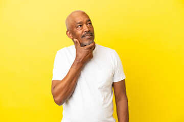 Cuban Senior isolated on yellow background thinking an idea while looking up