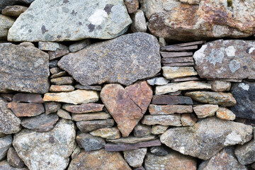 Heart-shaped stone stuck in the middle of a wall with other small and large stones - Powered by Adobe