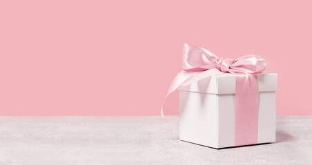 White gift box with shining pink ribbon bow on pink background. Gift or holiday concept. Mothers...