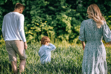 Fototapeta premium Happy family of young farmers and their son are walking in the field with lush green grass. back View . Farming concept