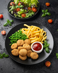 Fried crispy chicken nuggets with ketchup, french fries and green peas in black plate