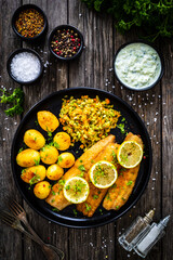 Fried herring fillets with potatoes and vegetable salad on wooden table
