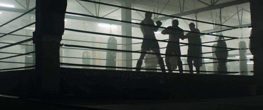 HANDHELD WIDE Two male fighters having kickboxing MMA sparring on a boxing ring. Trainers cheering. Shot with 2x anamorphic lens