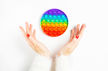 Female hands with red manicure hold silicone flexible anti-stress pop or simple dimple in palms on white background