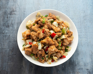 Stir fry chinese salt and pepper chicken with red, green chilli, onion, spring onion in white bowl.
