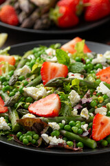 Asparagus and Strawberry Salad with vegetables, green peas and feta cheese in black plate. healthy food.