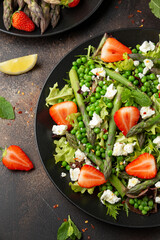 Asparagus and Strawberry Salad with vegetables, green peas and feta cheese in black plate. healthy food.