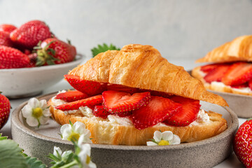 Croissants with fresh strawberries and cream cheese in a plate with flowers for tasty breakfast. close up