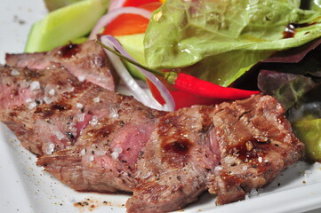 Delicious portion of healthy grilled lean medium rare beef steak cut through and served on white plate garnished with salad
