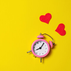 Pink alarm clock with red hearts on yellow background, top view, copy space.