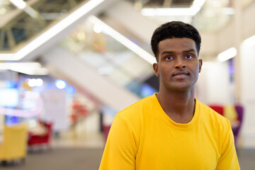 Portrait of handsome black African man wearing yellow t-shirt in shopping mall