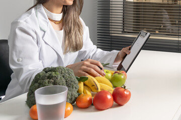 Smiling female nutritionist in her office, writing diet plan showing healthy vegetables and fruits. Healthcare and diet concept. Lifestyle.