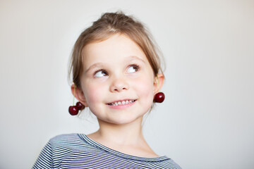 Pretty little girl with cherry earrings on bright background