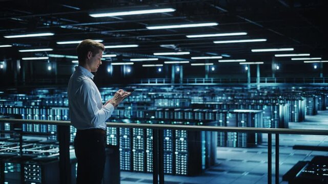 Data Center Specialist Engineer Using Tablet Computer. Server Farm Cloud Computing Facility with System Administrator Working. Data Protection Network for Cyber Security. Static Wide Medium