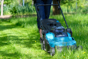 Female cutting grass using lawn mower. Maintenance garden