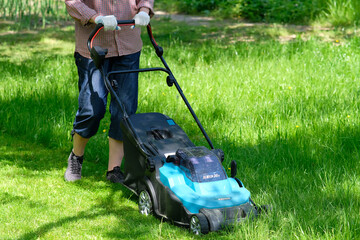 Woman using electric lawn mower for cutting grass.