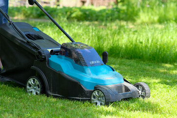 Garden electric lawn mower cutting grass, closeup view. - obrazy, fototapety, plakaty