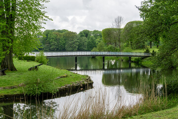 Obraz premium idyllic and peaceful park next to a pond wth green summer trees and a bridge leading across