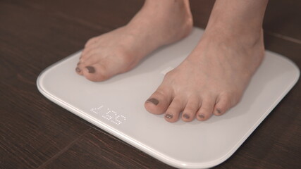 The girl gets on the scales. Weighing on scales. Close-up of female legs on the scales. Excess weight check