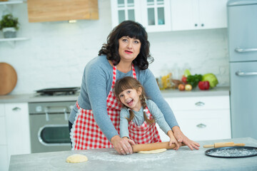 Grandmother and granddaughter cook pizza together, roll the dough with a rolling pin. Family culinary traditions