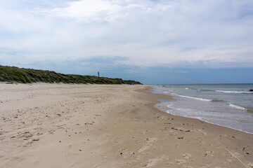 beautiful white sand beach with a lighthouse in the background high up on grassy sand dunes