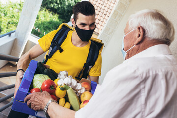 Young male volunteer in mask delivering shopping to senior man. Donation