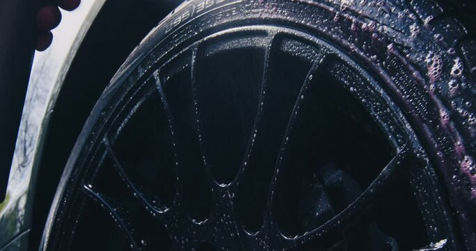 Car washing and detailing. Close up of cleansing wheels. Male hand spraying water and soap on wheel surface
