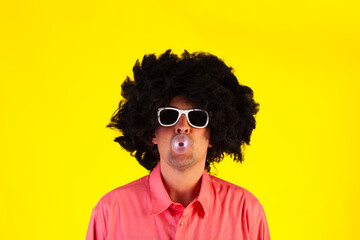 Fototapeta na wymiar Curly man wearing sunglasses blowing bubble with chewing gum