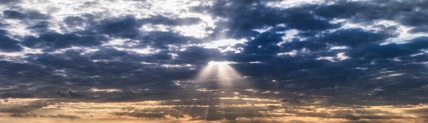 Panorama of orange and dark blue dramatic sky with clouds at sunset, summer evening. The sun's rays break through the dark clouds. Blur in motion.