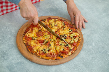 Someone is cutting the finished pizza into sections of the sector for the whole family. Close-up of pizza on the kitchen table.