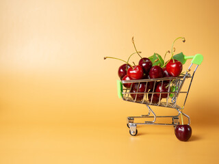 A supermarket cart filled with ripe red cherries on an orange background. Close-up