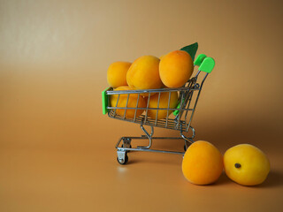 A supermarket cart filled with ripe apricots on a beige background. Close-up