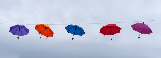 colorful umbrellas hanging on a cable underneath an expressive overcast sky