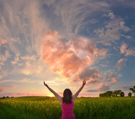 Joyful woman spreads her arms towards big heart in heaven