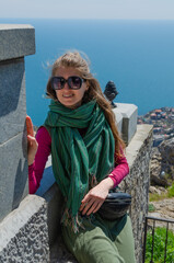 A young woman enjoys the scenic view of the mountains, sea and flowering trees. Spring in the Crimea. Vacation and travel concept.