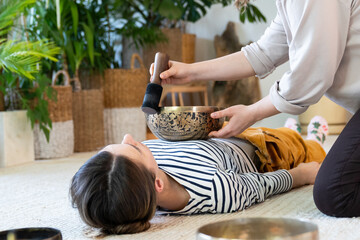 Young female having tibetan massage, singing bowl therapy with traditional tibet cymbals at home. Caucasian woman relax with alternative buddhism medicine. Wellbeing, wellness, stress relief concept - obrazy, fototapety, plakaty