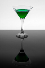 Green liquid in martini glass on white background. Mirror reflection on a black table