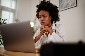 Displeased black healthcare worker using computer and reading an e-mail at doctor's office.