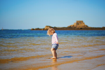 Fototapeta na wymiar Еoddler girl having fun on the beach in Saint-Malo, Brittany, France