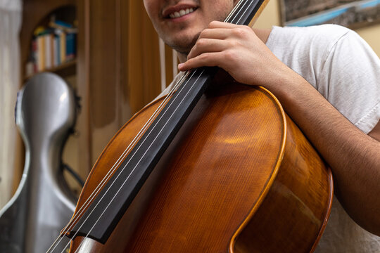 young girl smiling before performing or rehearsing the musical piece with the cello inside the house where the cello case can be seen in the background.
