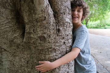 An happy 9 years old kid embracing a big tree. Sustainability concept of children loving nature.