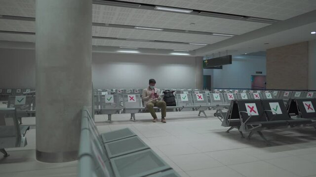 Waiting for flight at empty airport in Cyprus. Man sitting on chair with social distance marker at empty Paphos terminal. Flights canceled during quarantine. Collapse of airlines at coronavirus