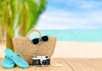 beach bag, flip flops, camera, sunglasses and starfish on wooden table. defocused palm trees and sea background