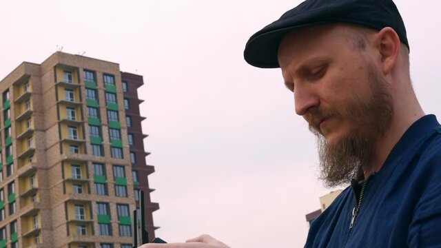 A man with a beard and a cap watches the drone's flight using the drone's flight controller. Aircraft control in the city.