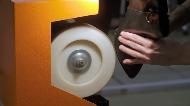 Shoemaker, shoes master using automatic shoe polish machine tool for polishing black leather women footwear at workshop - close up