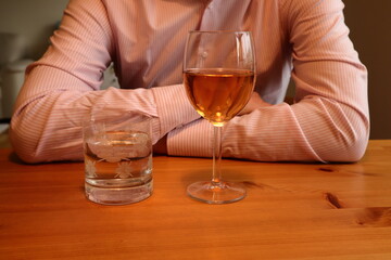 Glass of rose wine and water. One man sitting down at a table with arms in cross. Nice shirt and wooden furniture. Sit or drink. Faceless photo. Stockholm, Sweden, Europe.